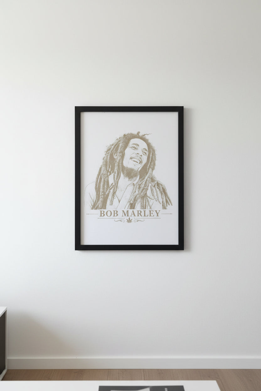 A white art print featuring a sepia-toned sketch portrait of Bob Marley with the text 'BOB MARLEY' and a small leaf emblem below, photographed resting on a gray textured fabric surface.