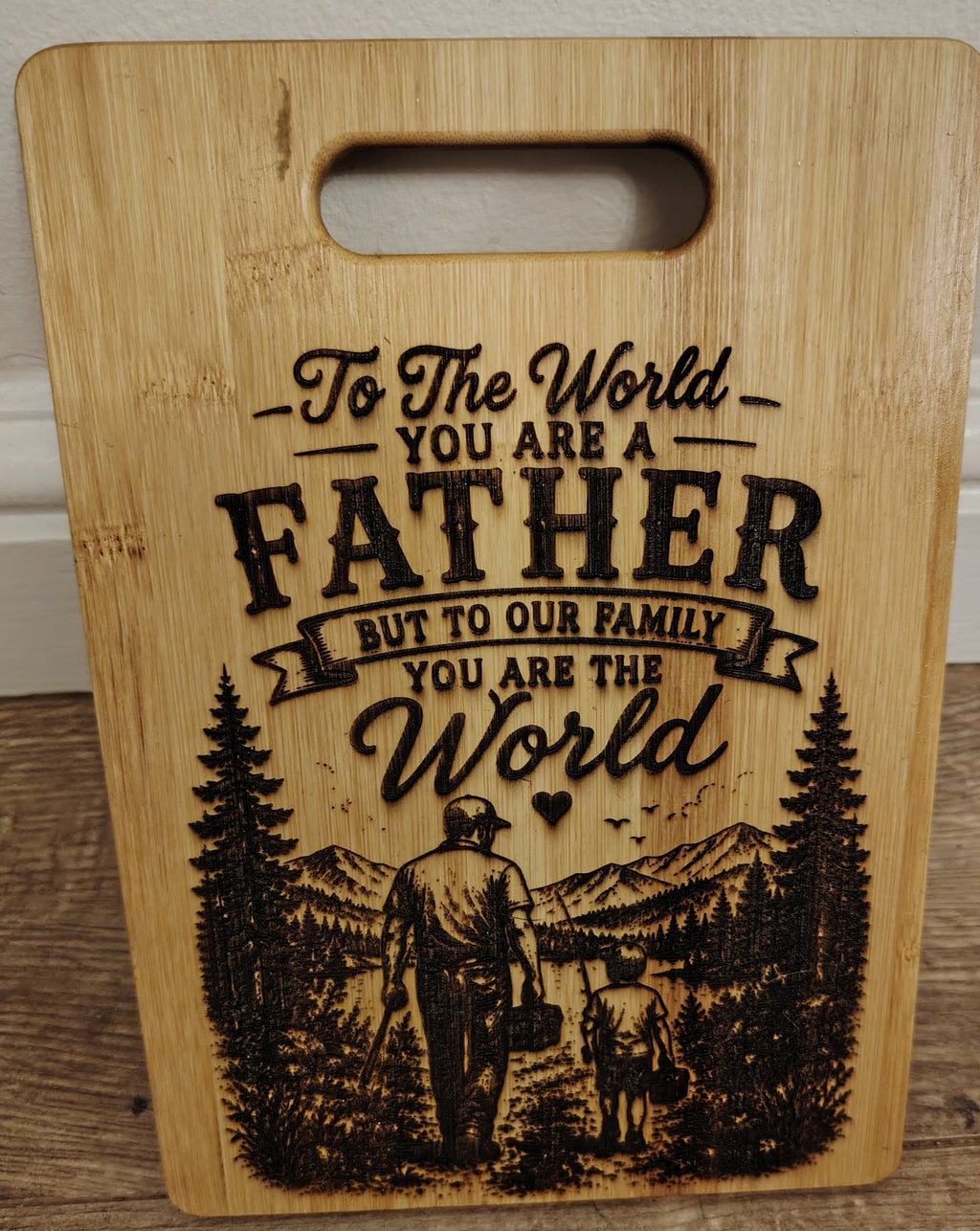 Wooden cutting board with engraved message and illustration of a father and child.
