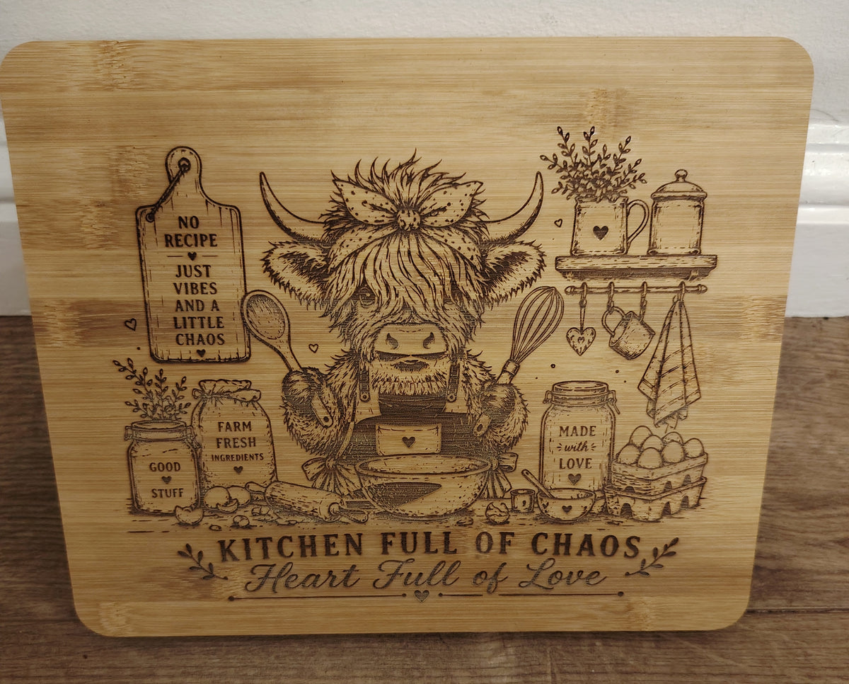 Wooden cutting board with engraved highland cow and kitchen-themed text on a wooden surface.