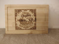 A rectangular light wood tray or cutting board with a recessed border and a laser-engraved Christmas illustration in the center. The design features Santa Claus in a sleigh pulled by reindeer under the words 'Merry Christmas,' surrounded by pine branches and snowflakes.