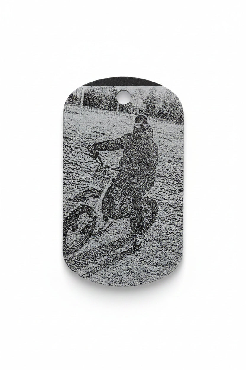 A small oval-shaped printed card or sticker showing a black-and-white photo of a person riding a dirt bike outdoors, placed on a light-colored surface with some glare and scratches visible.